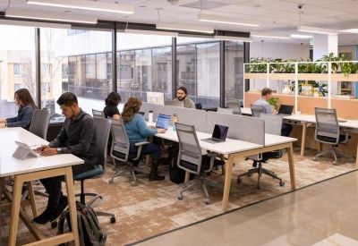 Spacious open-plan workspace with professionals at desks near large windows.