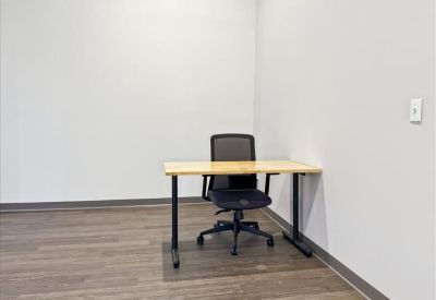 Minimalist private office with a light wood desk and black ergonomic chair.