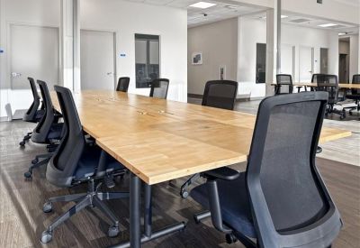 Long wooden conference table with several black mesh chairs in a bright meeting space.