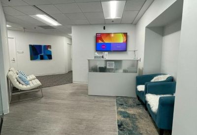 Reception lobby with a white front desk, teal armchairs, and a wall-mounted TV.