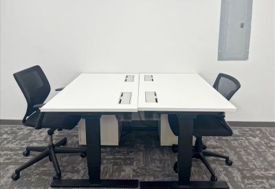 Two-person workspace featuring white sit-stand desks and ergonomic black mesh chairs.