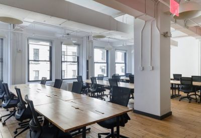 Open-plan workspace with long light-wood desks and black ergonomic chairs.