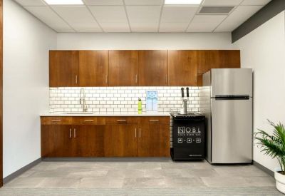 Breakroom kitchen with wood cabinets, subway tile backsplash, and a full-size stainless steel refrigerator.