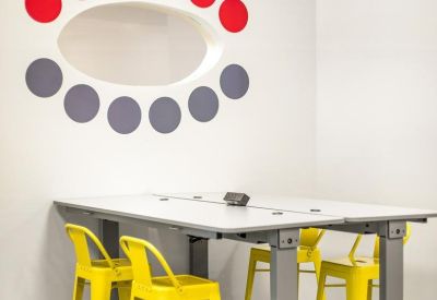 Bright breakout space featuring a modern wall graphic, high table, and vibrant yellow bar stools.