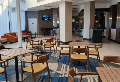 Modern hotel-style lobby lounge with various wooden tables and chairs on a patterned blue carpet.