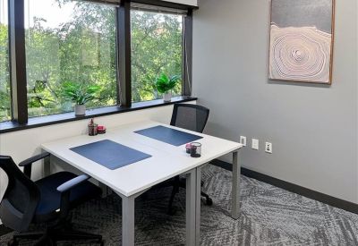 Private office with a white L-shaped desk and a window overlooking green trees.