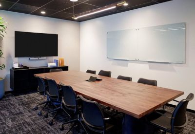 Executive conference room with a large wood table, black chairs, and a glass whiteboard.