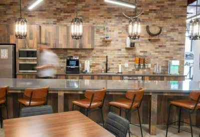 Communal kitchen area with rustic wood-paneled walls, leather bar stools, and industrial pendant lighting.