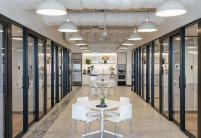 Long corridor with glass-walled private offices and a central breakout table.