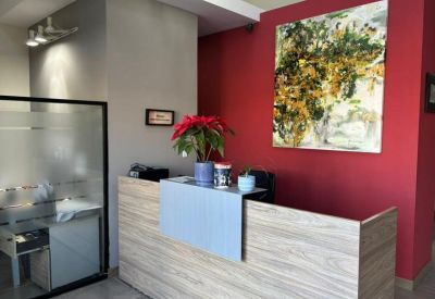 Bright reception area featuring a wood-panel desk, red accent wall, and colorful floral artwork.