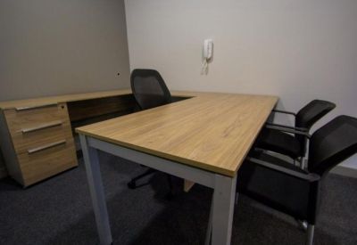 Private office suite with a wood-finish L-shaped desk and black mesh chairs.