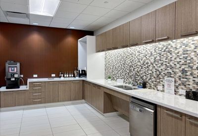 Modern office kitchen with wood-look cabinetry and a mosaic tile backsplash.