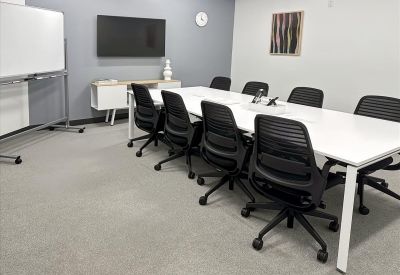 Spacious boardroom at 11900 Biscayne Boulevard with a large white table, black chairs, and a mounted TV screen.