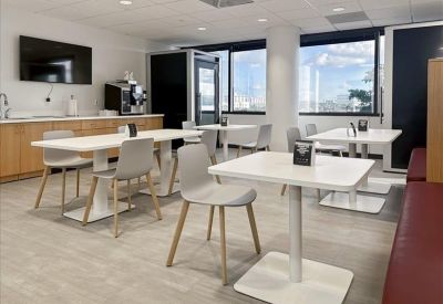 Modern communal kitchen and dining area with white tables, grey chairs, and a coffee station.