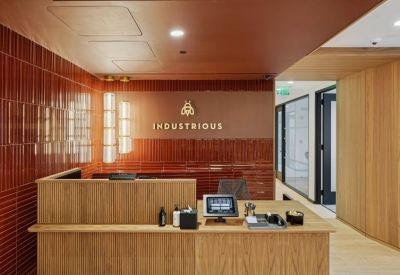 Wooden reception desk against a red tiled wall with gold Industrious branding.