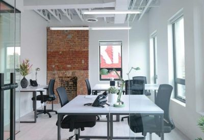 Bright open-plan workspace with white desks, ergonomic chairs, and an exposed brick feature wall.
