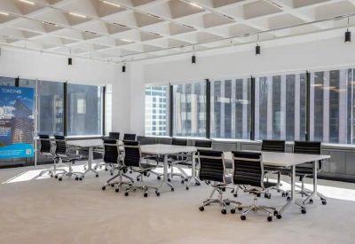 Bright coworking space featuring several white tables and black ergonomic chairs.