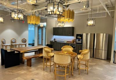Communal kitchen area with a high-top table, golden chairs, and stainless steel refrigerators.