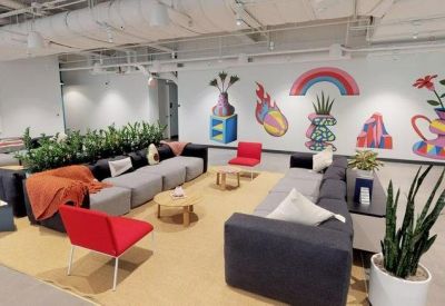 Bright lounge area with colorful wall murals, grey sectional sofas, and red accent chairs.