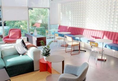 Modern breakout space with a long pink banquette, colorful chairs, and floor-to-ceiling windows.