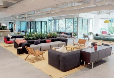 Expansive open-plan office lounge with multiple seating clusters, indoor plants, and high ceilings.