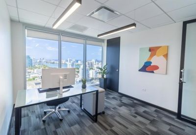 Private corner office with a glass desk, abstract wall art, and panoramic city views.