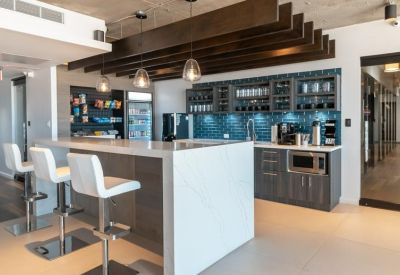Modern office kitchen with a white marble island, dark cabinetry, and blue tile backsplash.