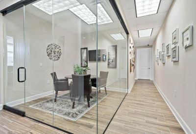 Modern glass-walled conference room with a wooden dining-style table and grey chairs.