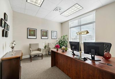 Bright professional workspace with a large wooden desk, guest chairs, and multiple windows.
