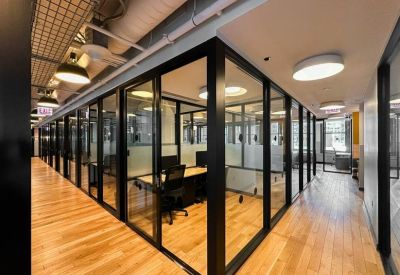 Glass-walled corridor leading to private office suites with wood flooring.