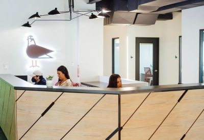 Reception desk with a light wood geometric design and a neon bird sign on the wall.