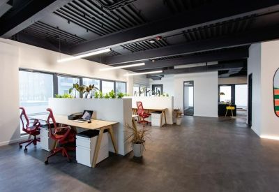 Bright open-plan workspace with white desks, red ergonomic chairs, and potted plants.