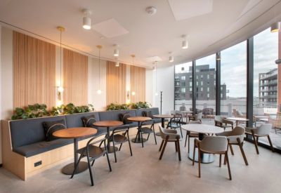 Sunlit cafe and lounge area with circular tables, curved booth seating, and floor-to-ceiling windows.