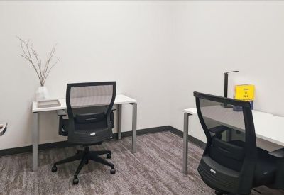 An internal two-person office suite featuring white desks and black mesh chairs.