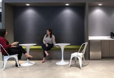 Communal breakout area featuring white bistro tables and a recessed green bench seat.