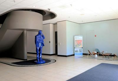 Spacious building lobby featuring a striking blue human-shaped sculpture and a curved architectural staircase.