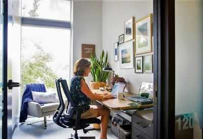 Private office suite with a person working at a desk beside a tall window.