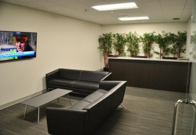 Waiting area with black leather sofas, a coffee table, and greenery along the back wall.
