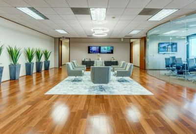 Bright lounge area with grey armchairs, indoor plants, and wood flooring.