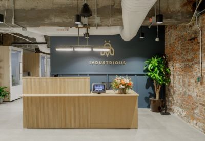 Reception area with a light wood slatted desk and Industrious branding on a navy wall.