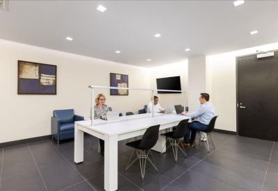 Bright communal coworking space with a large white table, partitioned workspace, and blue lounge chair.
