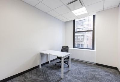 Private windowed office featuring a white desk, black chair, and grey patterned carpet.