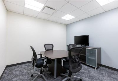 Small meeting room with a dark wood table, four ergonomic chairs, and a wall-mounted TV.