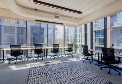 Bright open-plan office with multiple workstations facing floor-to-ceiling windows with city views.