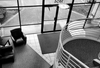 High-angle view of a modern building lobby with a curved staircase and black armchairs.