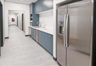 Modern office breakroom featuring blue cabinetry and a large stainless steel refrigerator.
