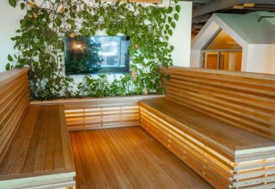 Lounge area with built-in wooden seating, a green plant wall, and a large TV screen.
