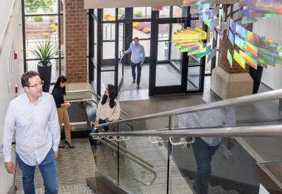 People walking through a modern multi-level office lobby with a glass staircase.