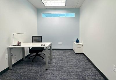 Private office with a white desk, black mesh chair, and a small transom window.