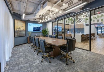 Professional boardroom featuring a long wood table, black leather chairs, and large glass partitions.